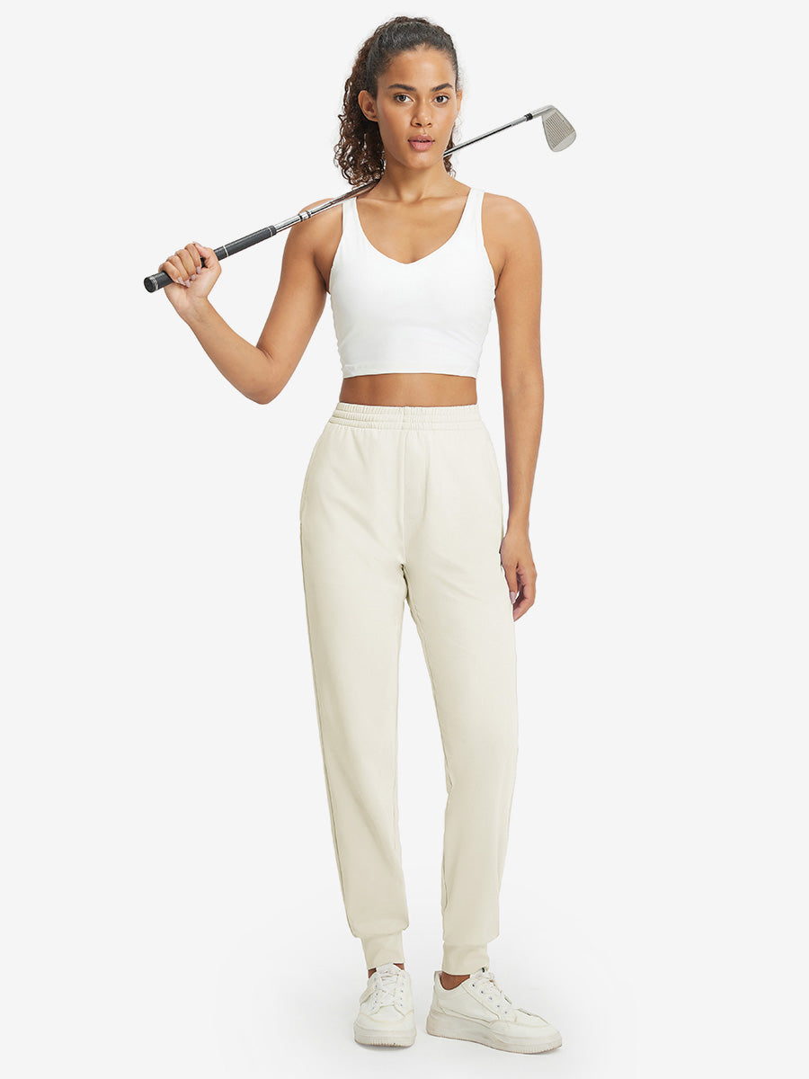 Model holding golf club behind neck while wearing lightweight women's stretchy joggers sweatpants in cream.