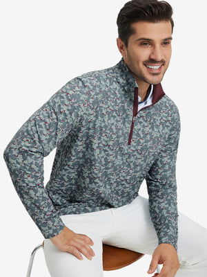 Model seated on chair, wearing full print quarter zip pullover in grey/wine camo, casual upper body view.