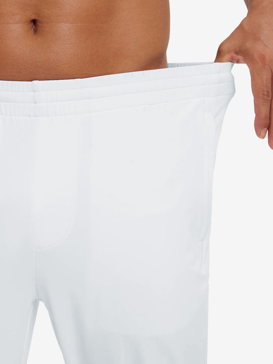 Model stretching waistband to show fit of lightweight traning track pants in white.