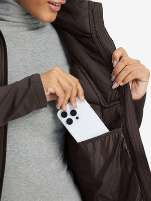 Hand placing an iPhone into pocket of women's lightweight fleece-lined puffer jacket in coffee brown.